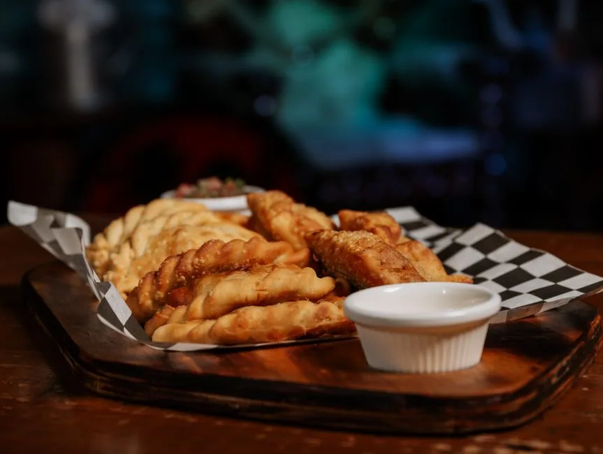 Deliciosas empanadas fritas dispuestas en una bandeja de madera con salsa para mojar.