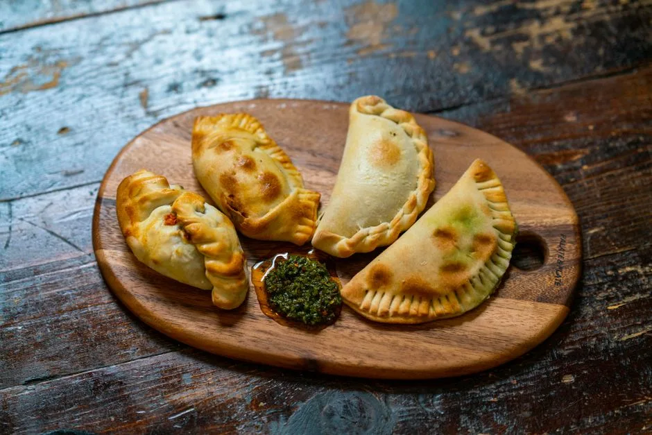 Empanadas al horno apetitosas servidas con salsa chimichurri sobre una tabla de madera. Perfecto para amantes de la comida.