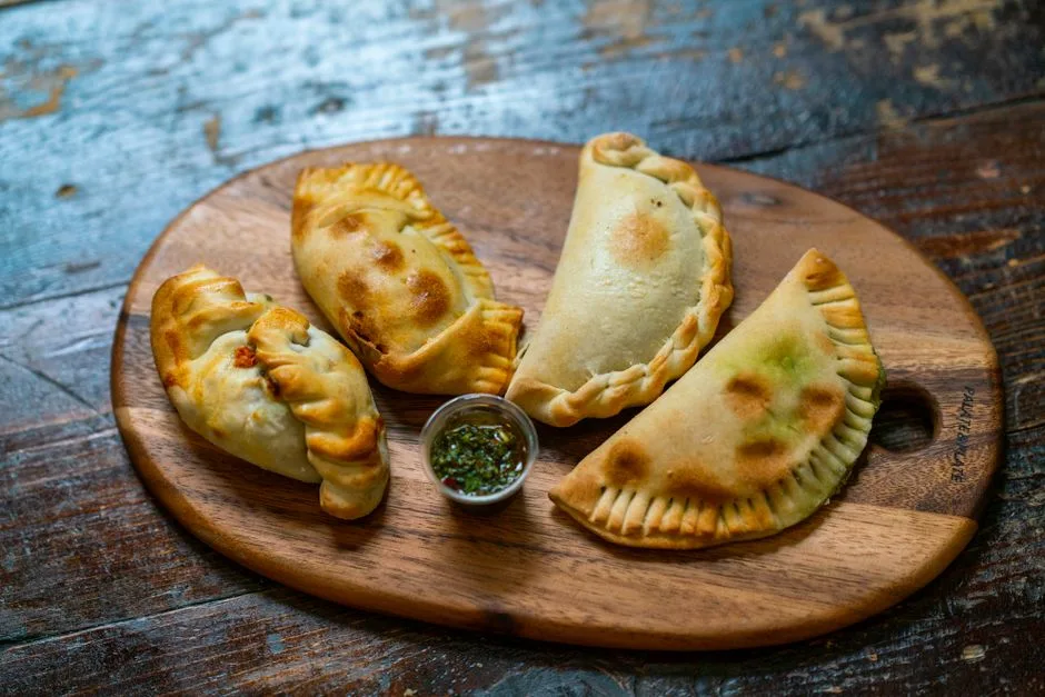 Sabrosas empanadas al horno sobre una tabla de madera con un dip, perfectas para los amantes de la cocina auténtica.