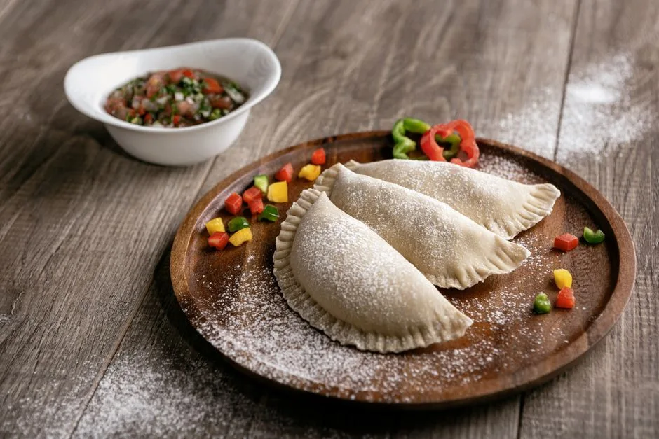 Tres empanadas en un plato de madera con azúcar en polvo, servidas con salsa para mojar en una mesa de madera.