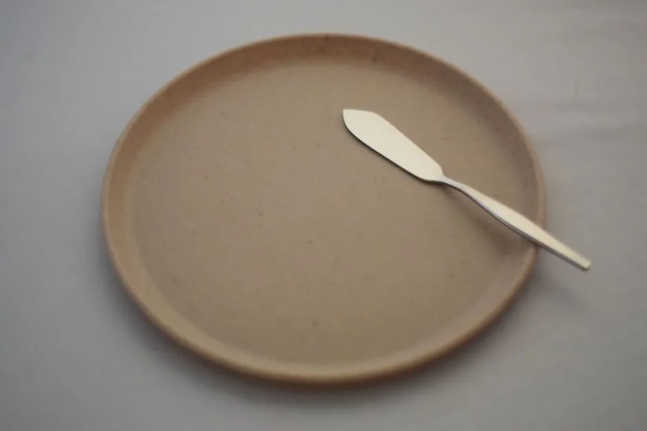 Un sencillo plato beige, acompañado de un cuchillo de mantequilla de acero inoxidable, sobre un suave mantel blanco.
