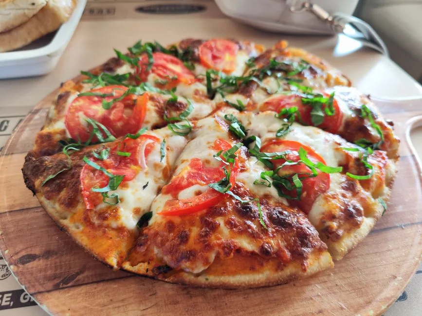 Primer plano de una pizza margarita recién hecha con tomate y albahaca. Perfecta para promociones de cocina italiana.