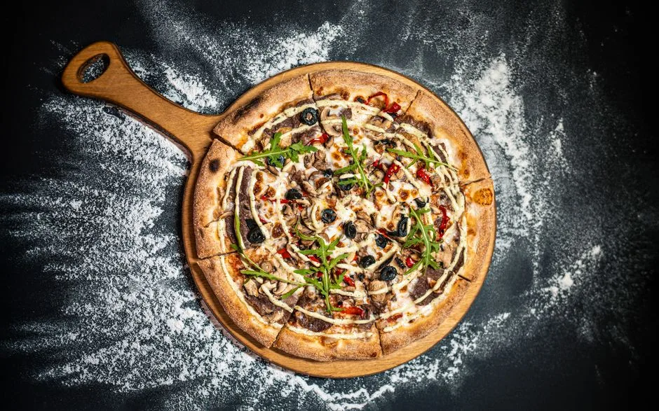 Deliciosa pizza al horno de leña con aceitunas, rúcula y pimientos sobre una tabla rústica.