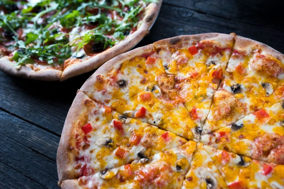 Un primer plano de dos pizzas irresistibles con ingredientes frescos sobre una mesa de madera.