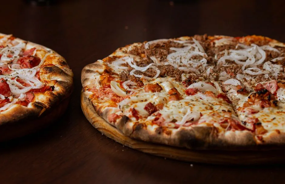 Primer plano de dos deliciosas pizzas con pepperoni y cebolla en una mesa de madera.