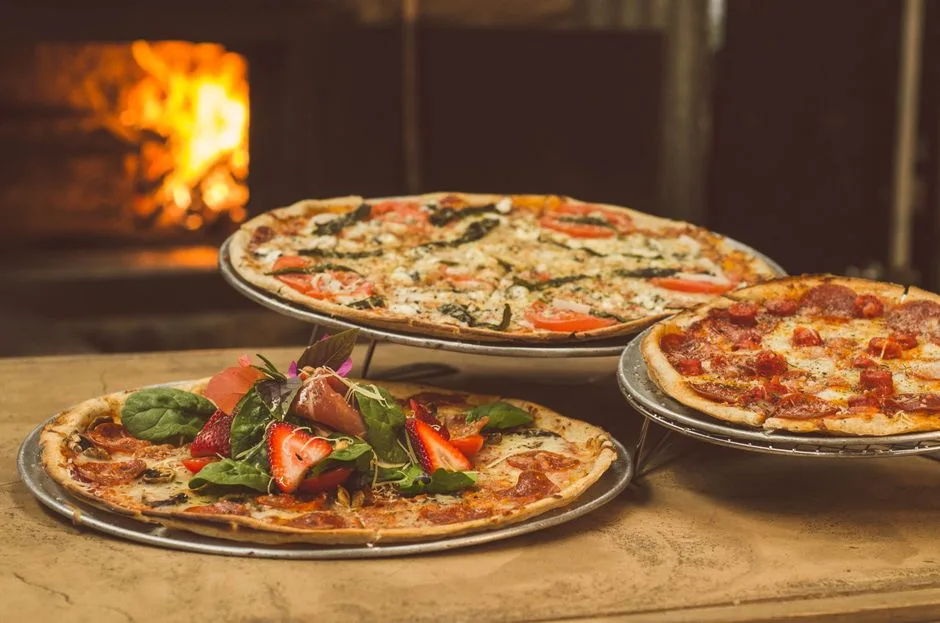 Trío de pizzas gourmet con coberturas únicas cerca de un horno de leña, ideal para amantes de la comida.