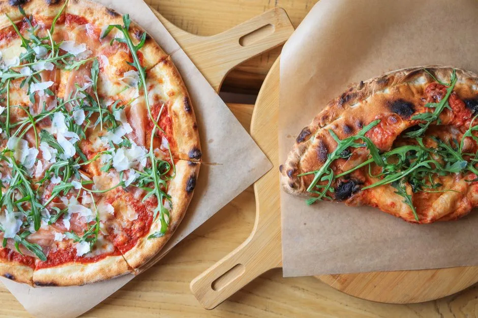 Pizzas recién horneadas cubiertas con jamón, rúcula y queso, servidas en tablas de madera.