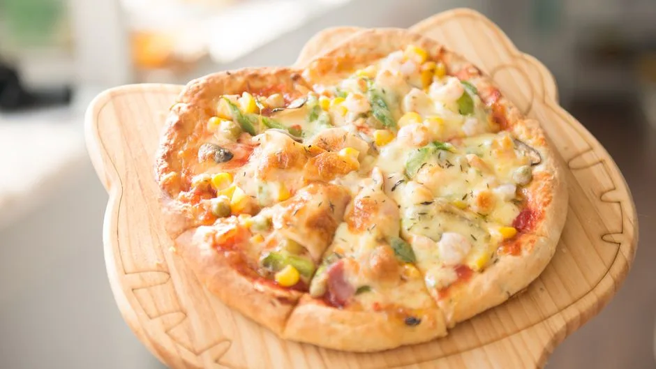 Pizza de verduras casera y fresca cubierta con queso, servida en una tabla de madera, perfecta para una comida gourmet.