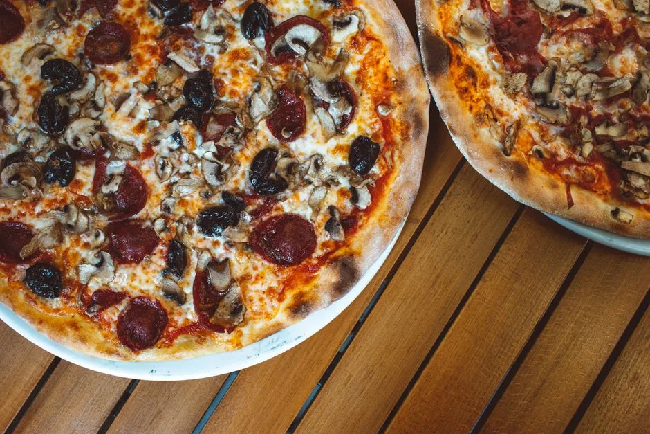 Primer plano de apetitosas pizzas de pepperoni y champiñones sobre una mesa de madera.