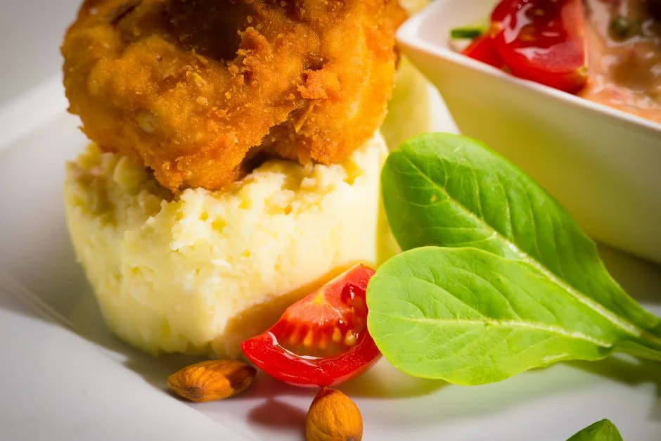 Primer plano de una comida reconfortante con pollo frito, puré de patatas y coberturas de ensalada frescas.