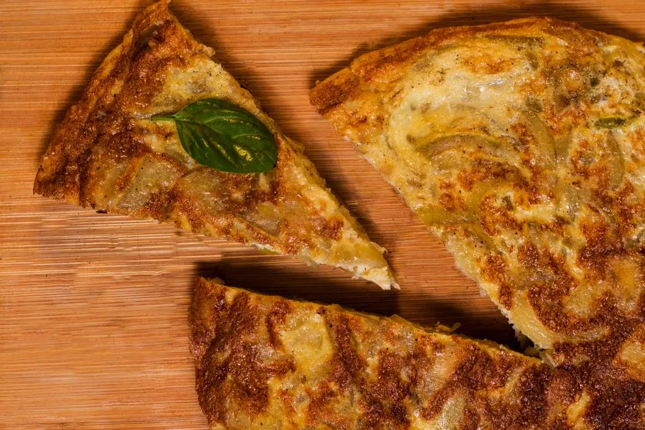 Acercamiento de rodajas tradicionales de tortilla española sobre una tabla de madera, adornadas con albahaca.